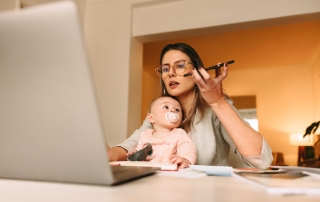 Working mother on a mobile while working on a laptop with a baby on her lap.