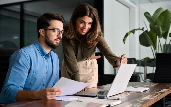 Manager supporting colleague in office using laptop